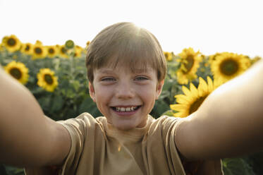 Fröhlicher Jugendlicher, der einen Moment in einem malerischen Sonnenblumenfeld mit einem Selfie festhält - ALKF00509