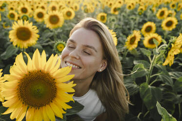 Lächelnde Frau mit geschlossenen Augen in der Nähe einer Sonnenblume auf einem Feld - ALKF00516