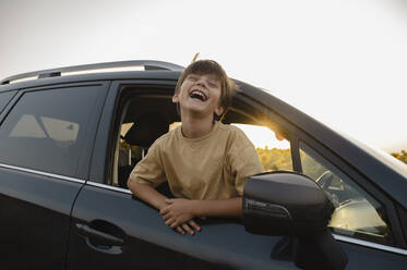 Cheerful boy leaning outside car window - ALKF00521