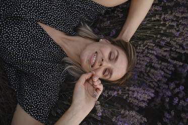 Woman with eyes closed lying on lavender flowers - ALKF00527