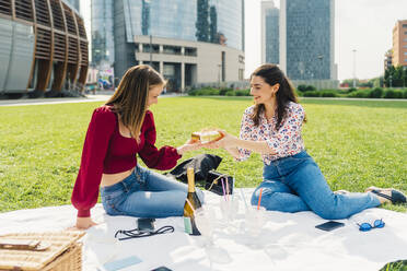 Glückliche Frau, die einem Freund ein Geschenk macht und ein Picknick im Park genießt - MEUF09164