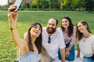 Eine fröhliche Frau hält einen Moment mit ihren Freunden fest, indem sie ein Smartphone für ein Selfie benutzt - MEUF09181