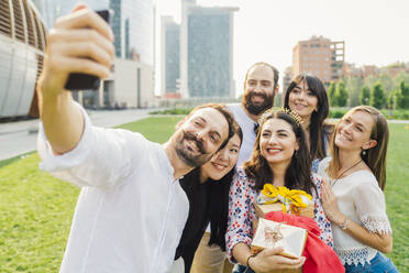 Eine Gruppe fröhlicher Freunde feiert einen Geburtstag in einem Park und hält den Moment mit einem Selfie fest - MEUF09203