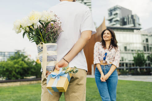 Man hiding gift box and bouquet of flowers in front of woman - MEUF09207