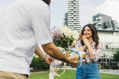 Mann gibt Geschenkbox und Blumenstrauß an glückliche Frau - MEUF09208