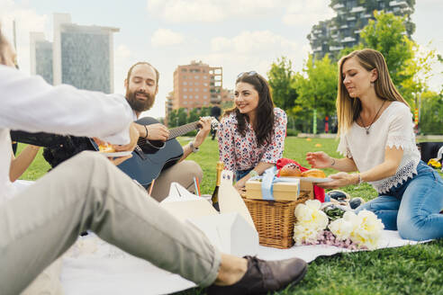 Lächelnder Mann spielt Gitarre mit Freunden beim Picknick im Park - MEUF09214