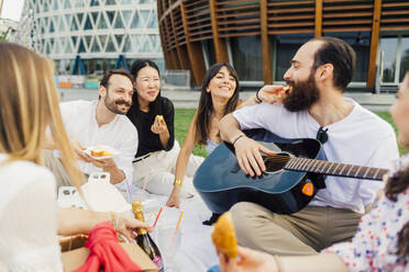 Glückliche Freunde, die zusammen Snacks essen und ein Picknick im Park genießen - MEUF09216