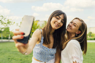 Zwei fröhliche Freunde halten einen Moment des Glücks in einem Park fest und posieren mit einem breiten Lächeln für ein Selfie - MEUF09222