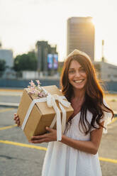Glückliche Frau mit Geschenkbox bei Sonnenuntergang - MEUF09248