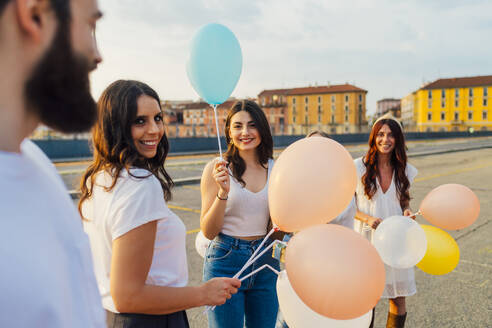 Glückliche Freunde stehen mit Luftballons und haben Spaß auf der Straße - MEUF09259