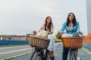 Glückliche Freunde fahren Fahrrad zusammen auf der Straße bei Sonnenuntergang - MEUF09279