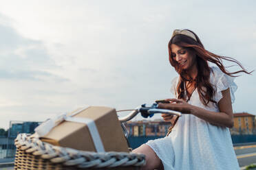 Happy woman using smart phone on bicycle at sunset - MEUF09280