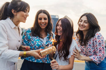 Happy woman giving gift to friend holding sparkler at sunset - MEUF09283