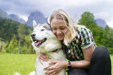 Lächelnde Frau mit geschlossenen Augen, die einen Husky-Hund umarmt - NJAF00482