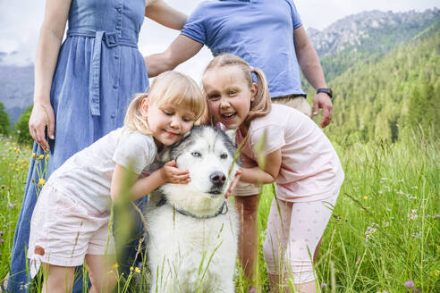 Niedliche Schwestern umarmen Hund auf Gras - NJAF00486