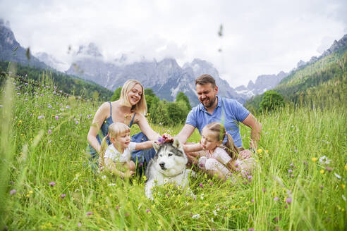 Familie genießt Urlaub mit Hund sitzt auf Gras vor Bergen - NJAF00490