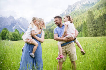 Vater und Mutter stehen mit ihren Töchtern vor den Bergen - NJAF00496