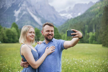 Smiling man taking selfie through smart phone with woman - NJAF00506