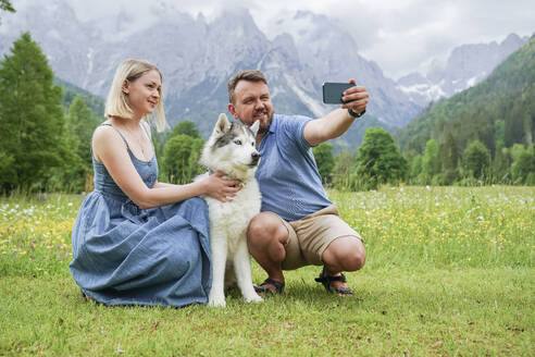 Ein Paar mit einem Husky-Hund hält einen schönen Moment in den Dolomiten, Italien, mit einem Selfie fest - NJAF00507