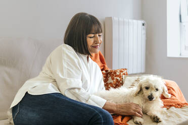 Lächelnde Frau streichelt Hund auf Bett zu Hause - PBTF00124