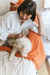 Senior woman stroking dog on bed at home - PBTF00125