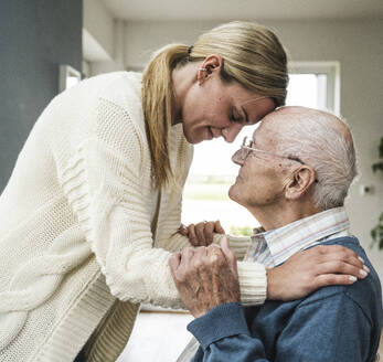 Lächelnde blonde Frau, die sich um ihren Vater kümmert und ihn zu Hause umarmt - UUF29900