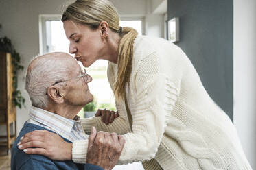 Blond woman kissing father on head at home - UUF29901