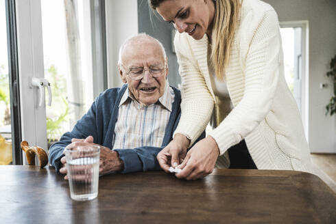 Happy woman giving medicine to father at table - UUF29907