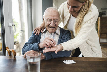 Blond woman giving medicine to father at table - UUF29908