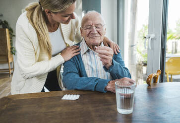 Glückliche Frau mit älterem Mann, der Medizin am Tisch hält - UUF29909