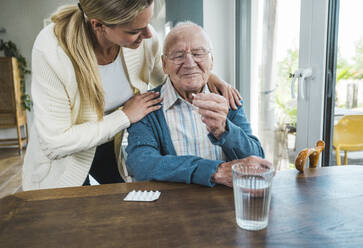 Happy woman with senior man holding medicine at table - UUF29909