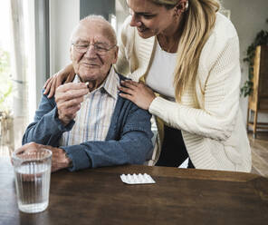 Lächelnde Frau mit älterem Mann, der Medikamente am Tisch hält - UUF29910