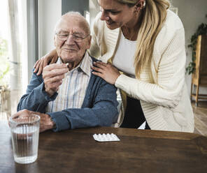 Smiling woman with senior man holding medicine at table - UUF29910