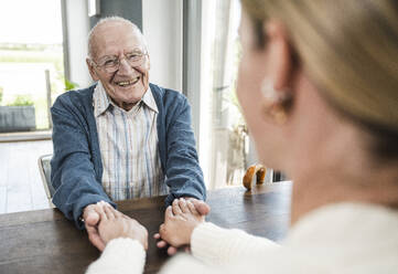 Happy senior man holding hands with daughter at home - UUF29914