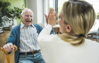 Happy senior man giving high-five to woman at home - UUF29919