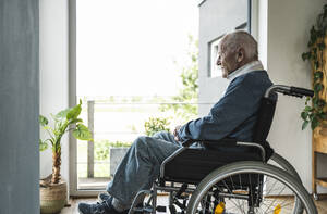 Älterer Mann sitzt im Rollstuhl am Fenster zu Hause - UUF29930