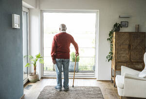 Kontemplativer älterer Mann vor einem Fenster stehend - UUF29938