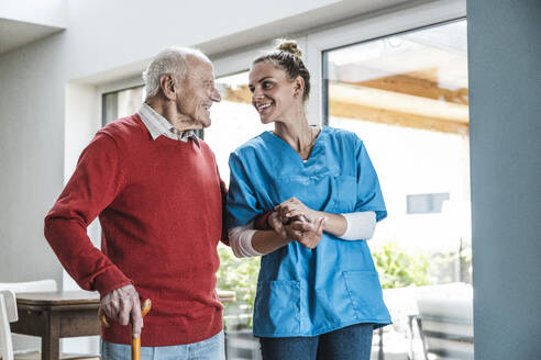 Happy senior man holding hands with nurse at home - UUF29945