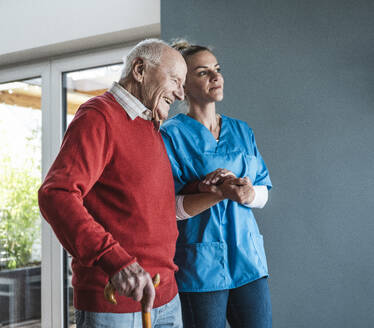 Lächelnde Krankenschwester, die sich um einen älteren Mann zu Hause kümmert und ihm die Hand hält - UUF29946