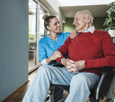 Glückliche Krankenschwester unterstützt und pflegt älteren Mann zu Hause - UUF29963