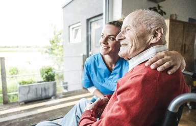 Glückliche Krankenschwester mit älterem Mann vor einem Fenster zu Hause - UUF29964