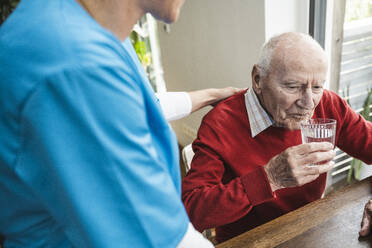 Nurse taking care of senior man drinking water at home - UUF29968