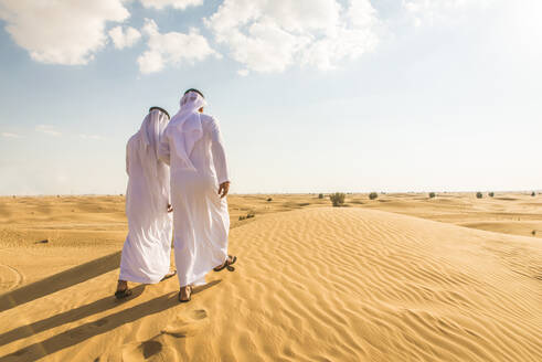 Arabian men witk kandora walking in the desert - Portrait of two middle eastern adults with traditional arabic dress - DMDF00390