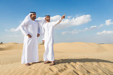 Arabische Männer mit Kandora beim Spaziergang in der Wüste - Porträt von zwei Erwachsenen aus dem Nahen Osten in traditioneller arabischer Kleidung - DMDF00393