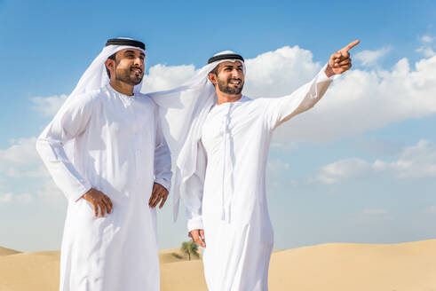 Arabische Männer mit Kandora beim Spaziergang in der Wüste - Porträt von zwei Erwachsenen aus dem Nahen Osten in traditioneller arabischer Kleidung - DMDF00394