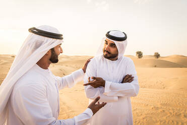 Arabische Männer mit Kandora beim Spaziergang in der Wüste - Porträt von zwei Erwachsenen aus dem Nahen Osten in traditioneller arabischer Kleidung - DMDF00416