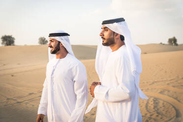 Arabische Männer mit Kandora beim Spaziergang in der Wüste - Porträt von zwei Erwachsenen aus dem Nahen Osten in traditioneller arabischer Kleidung - DMDF00420