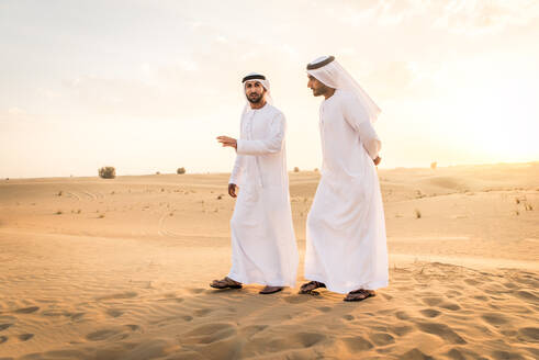 Arabische Männer mit Kandora beim Spaziergang in der Wüste - Porträt von zwei Erwachsenen aus dem Nahen Osten in traditioneller arabischer Kleidung - DMDF00425