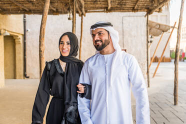 Arabisches Paar mit traditionellem emiratischem Kleid, das sich im Freien verabredet - Glückliches mittelöstliches Paar, das Spaß hat - DMDF00435