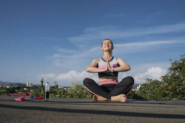 Smiling woman with crossed legs doing yoga on rooftop - OSF01922